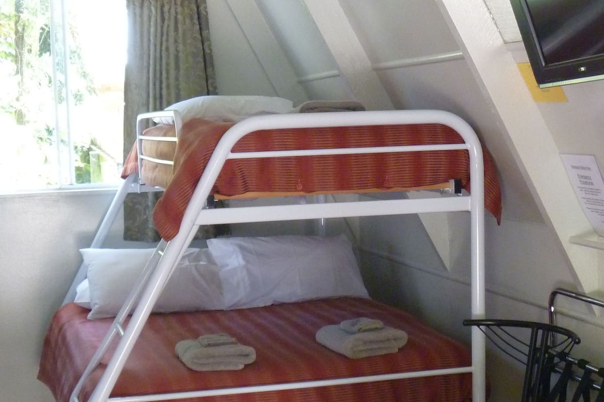 A dormitory room with bunk beds, a television, and a window with curtains.