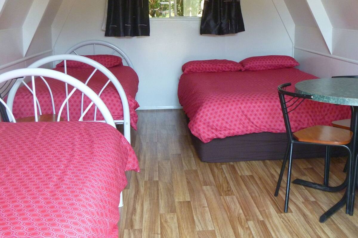 A compact room with two beds, a small table, and a chair.