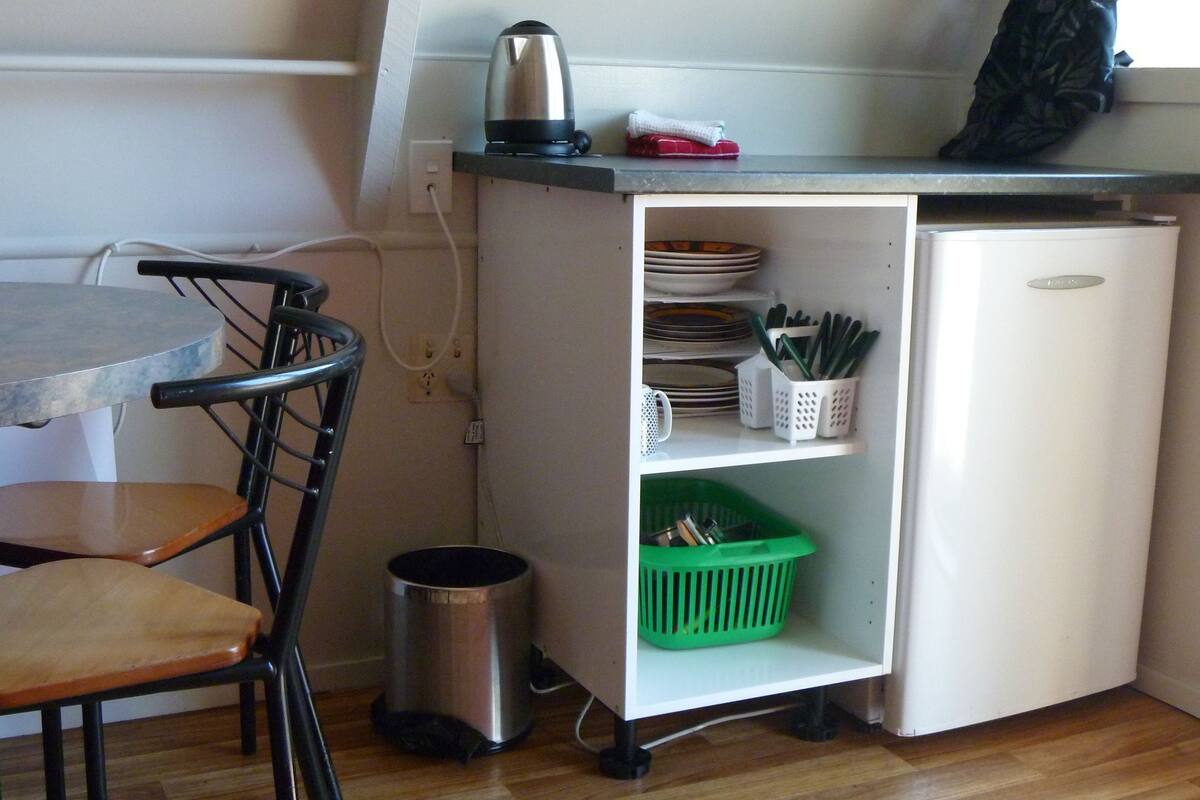 A compact kitchenette with a small fridge, a coffee maker, and a trash bin.