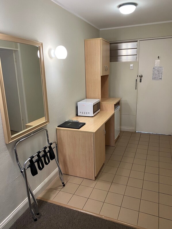 Una kitchenette compacta con microondas, un mueble pequeño y un espejo.