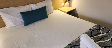 A neatly made bed with white linens, a teal pillow, and a towel on a patterned rug.