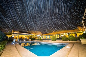 Una piscina con vistas a estelas de estrellas en el cielo nocturno, rodeada por un edificio con un porche cubierto.