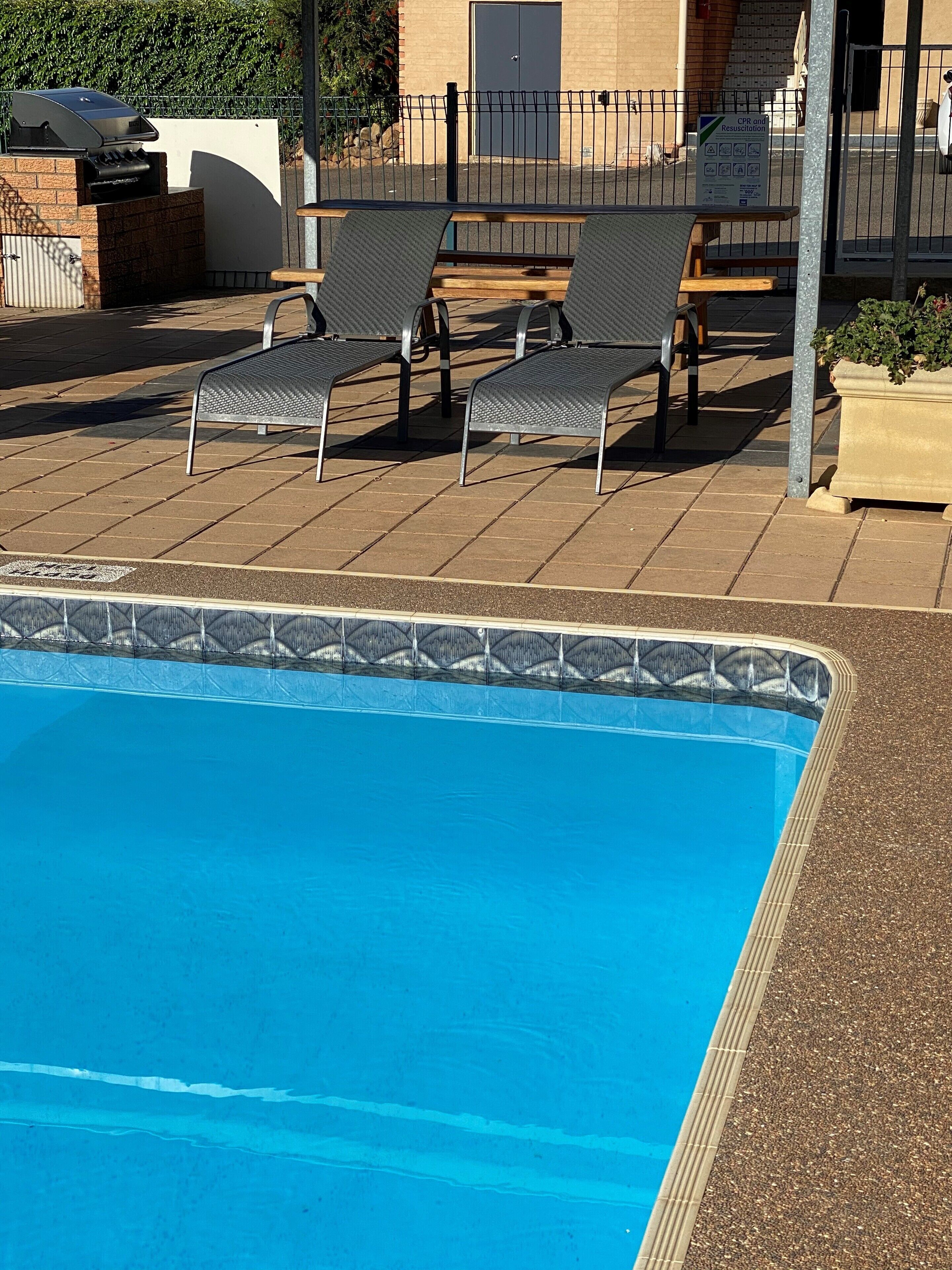 Una piscina con sillas de descanso y un muro de ladrillo al fondo.