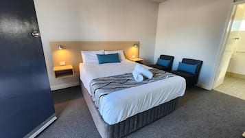 Quarto de hotel com cama grande, duas mesas de cabeceira, cabeceira e uma porta.