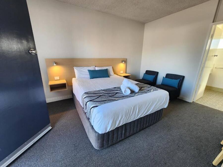 Quarto de hotel com cama grande, duas mesas de cabeceira, cabeceira e uma porta.