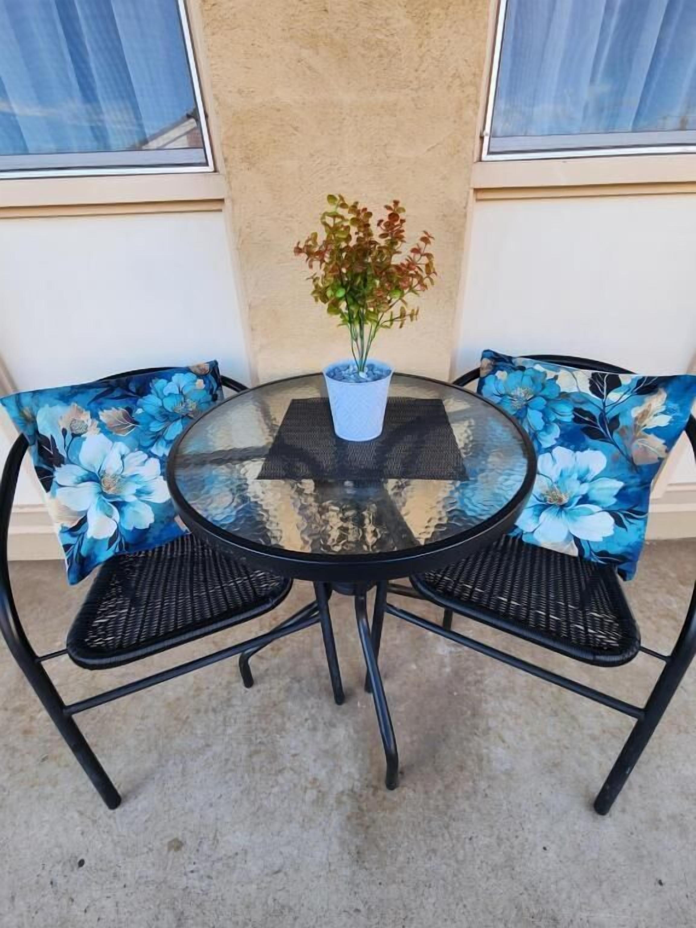 A round glass table with a potted plant, surrounded by chairs with floral upholstery.