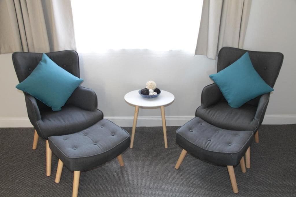 Two grey armchairs with blue cushions and a small white table with a decorative item between them.