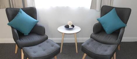 Two grey armchairs with blue cushions and a small white table with a decorative item between them.