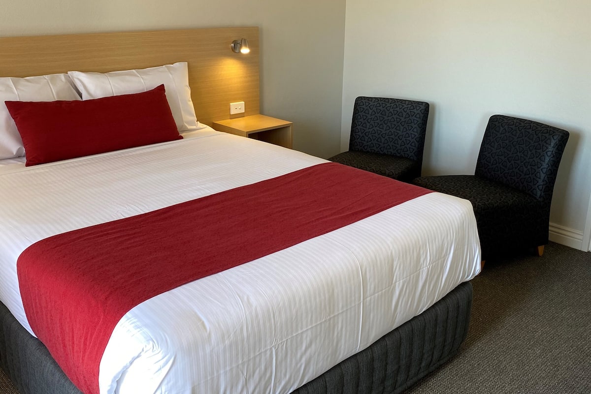 A hotel room with a large bed, a nightstand, two chairs, and a wall-mounted light.