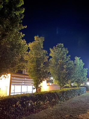 A nighttime view of a landscaped area with trees and a building with illuminated windows. - Country Gardens Motel (Coonabarabran)
