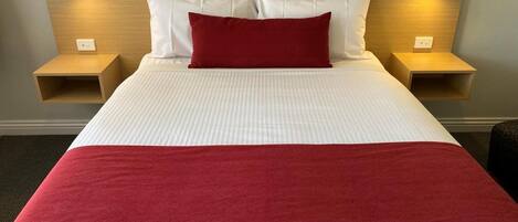 Una habitación de hotel con una cama grande, ropa blanca de cama, un plaid rojo y dos mesitas de noche con lámparas.