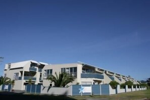 A modern multi-story building with balconies, a flat roof, and a gated entrance. - Marine Reserved Holiday Apartments (Whangamata)