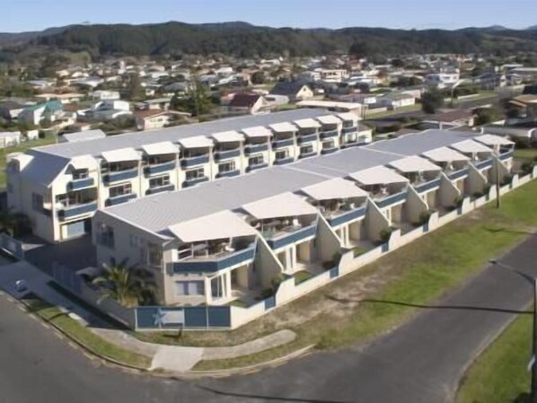 A row of modern, multi-story hotel buildings with balconies, set in a residential area with hills in the background. - Marine Reserved Holiday Apartments (Whangamata)