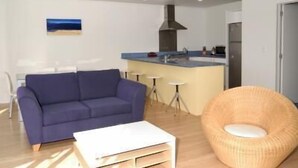 A modern living room with a sofa, a coffee table, and a wicker chair. - Marine Reserved Holiday Apartments (Whangamata)