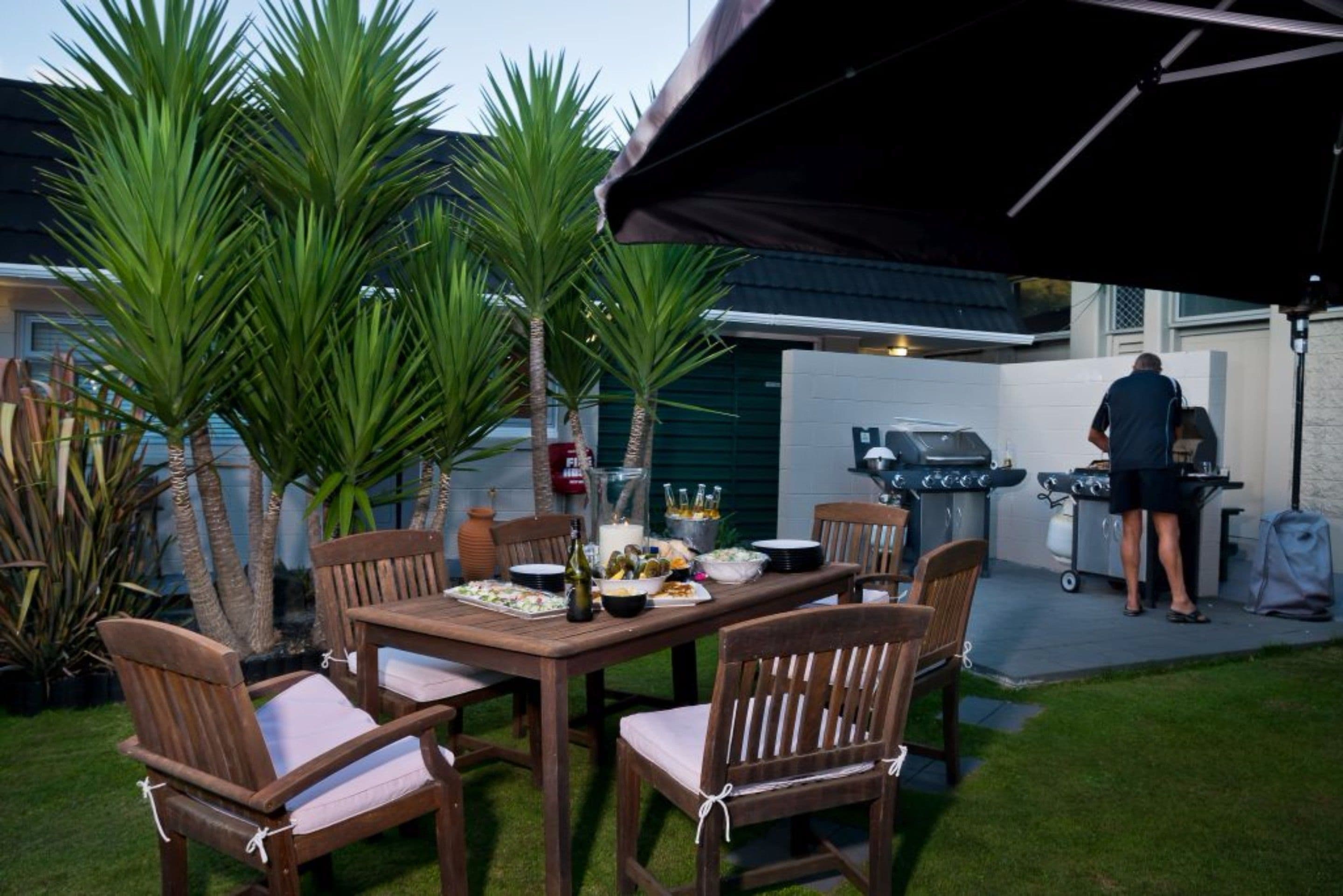 An outdoor dining area with a wooden table and chairs, a grill, and a fire extinguisher.
