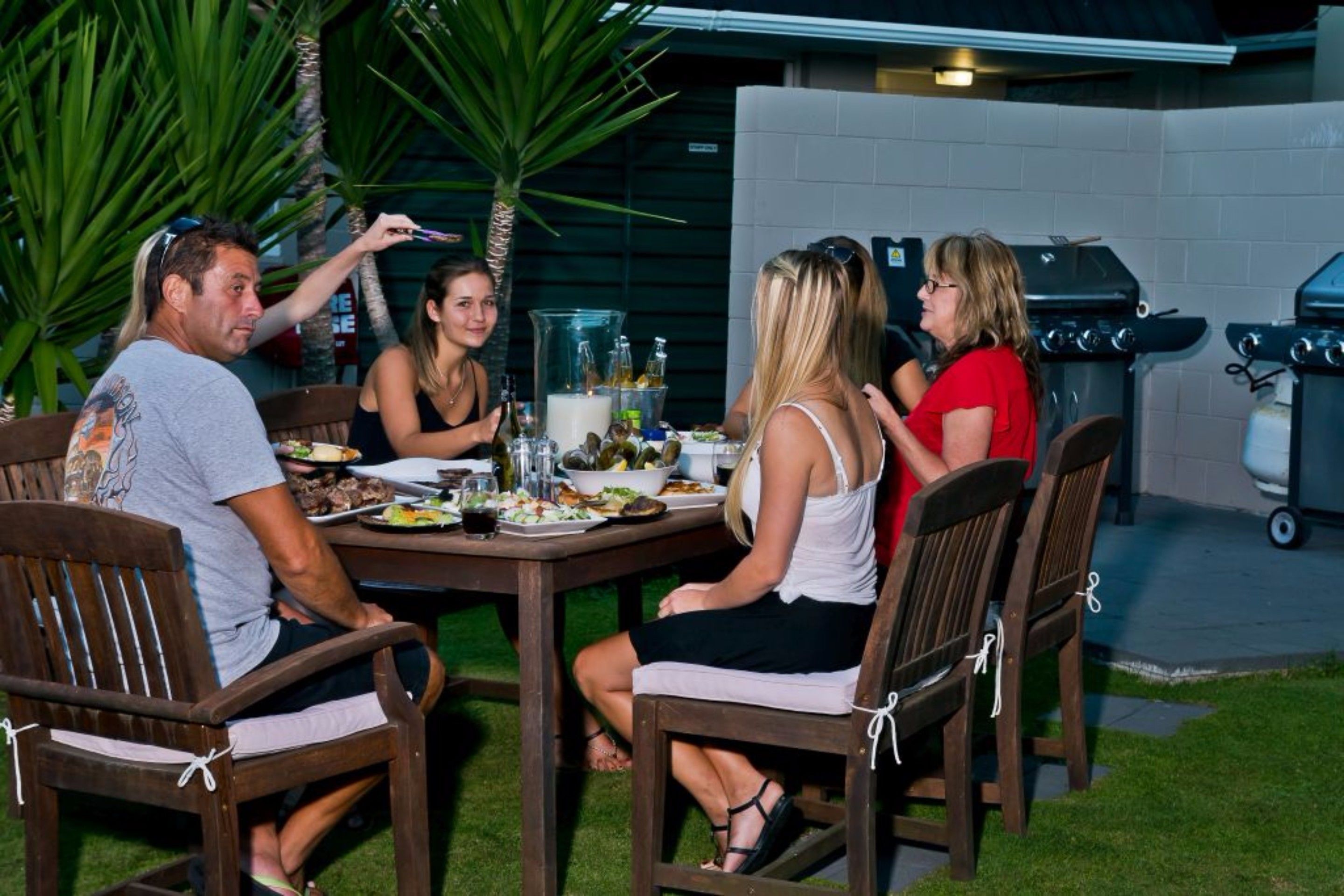 A group of people dining at an outdoor table with a grill in the background.