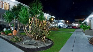 A well-maintained outdoor area with a paved walkway, green lawn, and various potted plants.