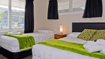 A hotel room with two beds, each with a green blanket, a bedside table with a lamp, and a window with black curtains.