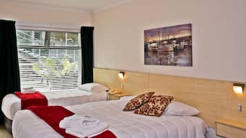 A hotel room with two beds, a painting of a harbor, and a window with blinds.