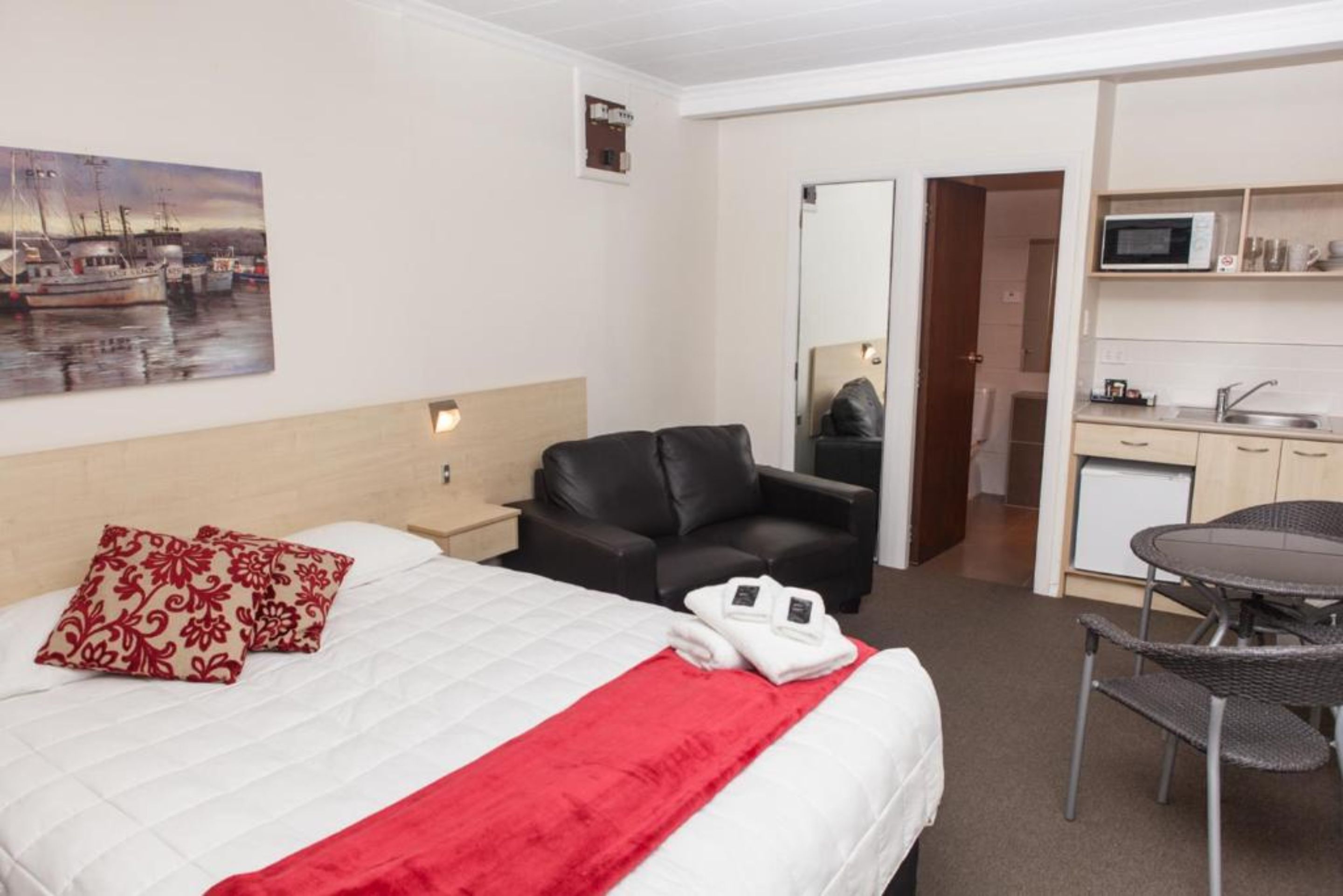 A hotel room with a bed, a desk, a chair, a microwave, and a small kitchenette.