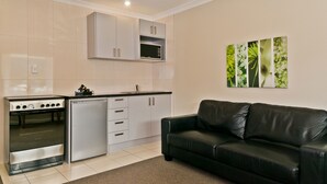 A compact kitchen with a built-in stove, microwave, and refrigerator, a black leather sofa, and a wall-mounted artwork.