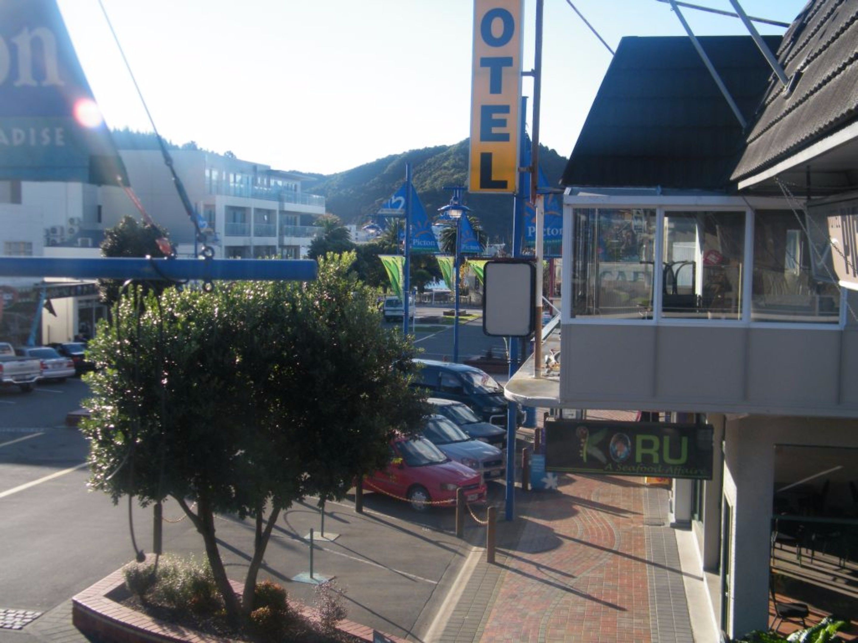 A hotel with a prominent 'HOTEL' sign, a small kiosk, and a parking area with cars.