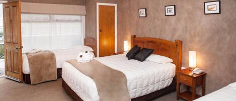 A hotel room with two beds, a wooden headboard, a bedside table with a lamp, and a door leading to a balcony.