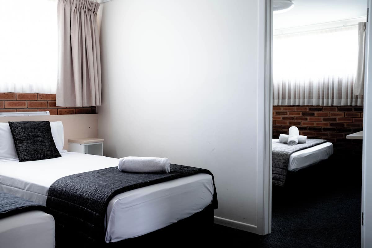 Una habitación de hotel con una cama grande, una cama más pequeña, una mesita de noche y una pared de ladrillo.