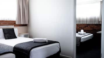 Une chambre d’hôtel avec un grand lit, un plus petit lit, une table de chevet et un mur en briques.