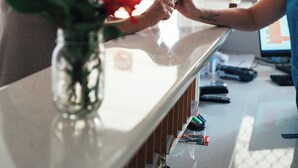 Un comptoir d’accueil avec une pancarte indiquant que l’établissement est ouvert, un vase avec une plante et une fenêtre avec des stores.