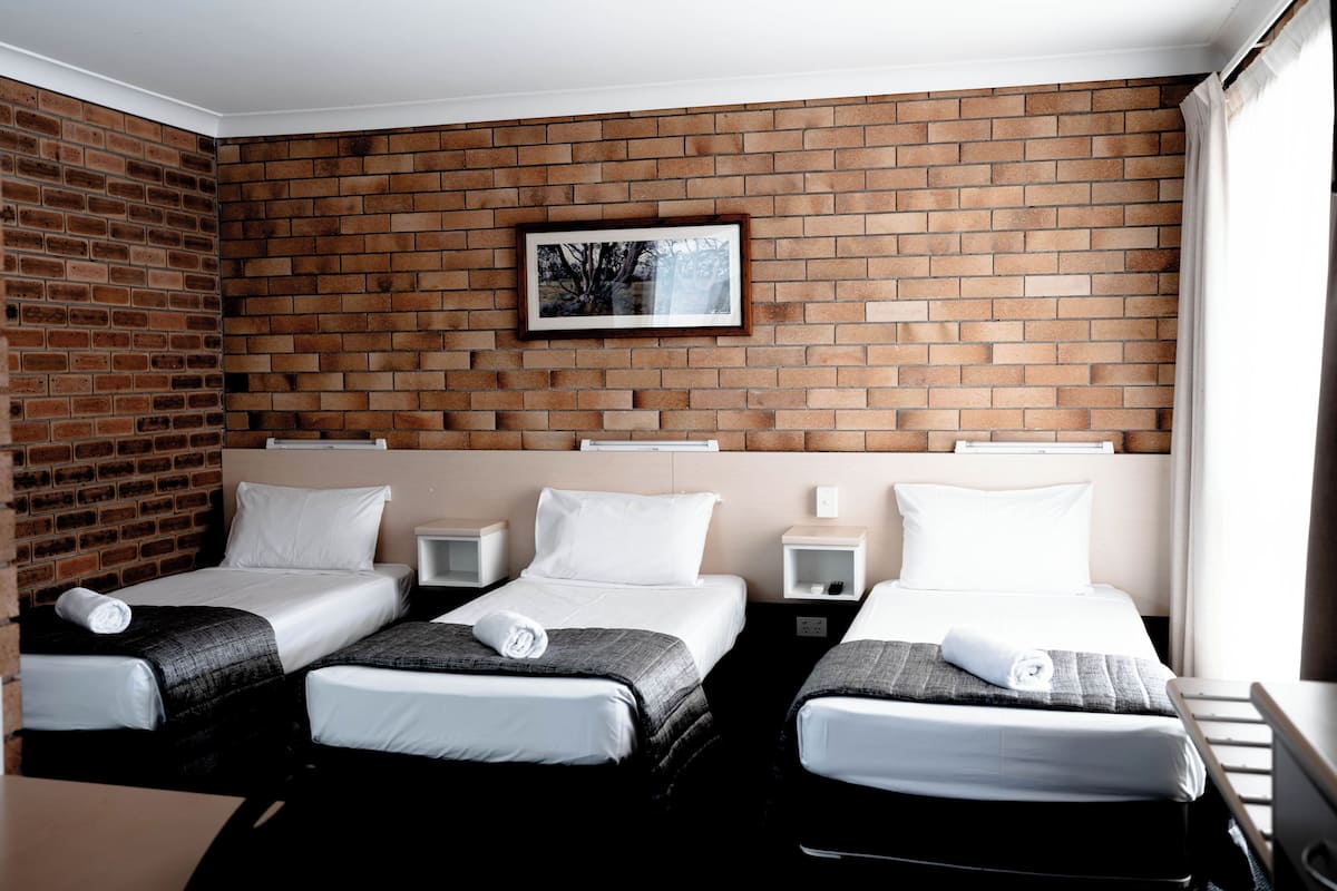 Habitación de hotel con dos camas individuales, una pared de ladrillo, un cuadro enmarcado y una ventana.