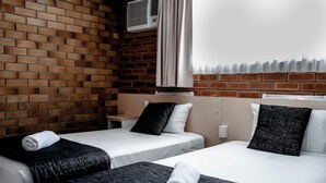 Une chambre d’hôtel avec deux lits, un mur en briques, un climatiseur et une fenêtre avec un rideau.