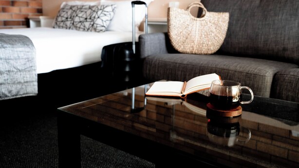 Une chambre d’hôtel avec un lit, un canapé, une table basse avec un livre et une tasse, et une valise.