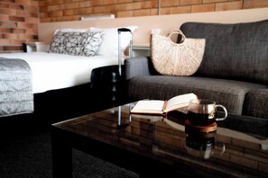Une chambre d’hôtel avec un lit, un canapé, une table basse avec un livre et une tasse, et une valise.