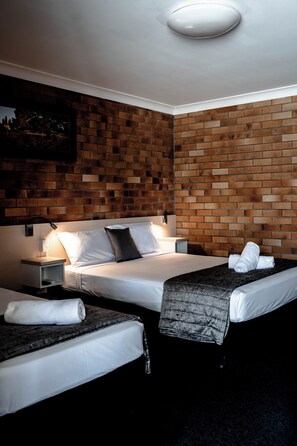 A hotel room with two single beds, a brick-patterned wall, a ceiling light, and a framed picture on the wall.