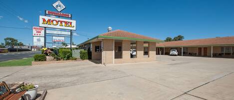 Un motel de la chaîne Buckaroo Inn, avec une allée d’accès dégagée, un espace de stationnement et un panneau indiquant les services proposés, tels qu’Apple TV et Netflix.