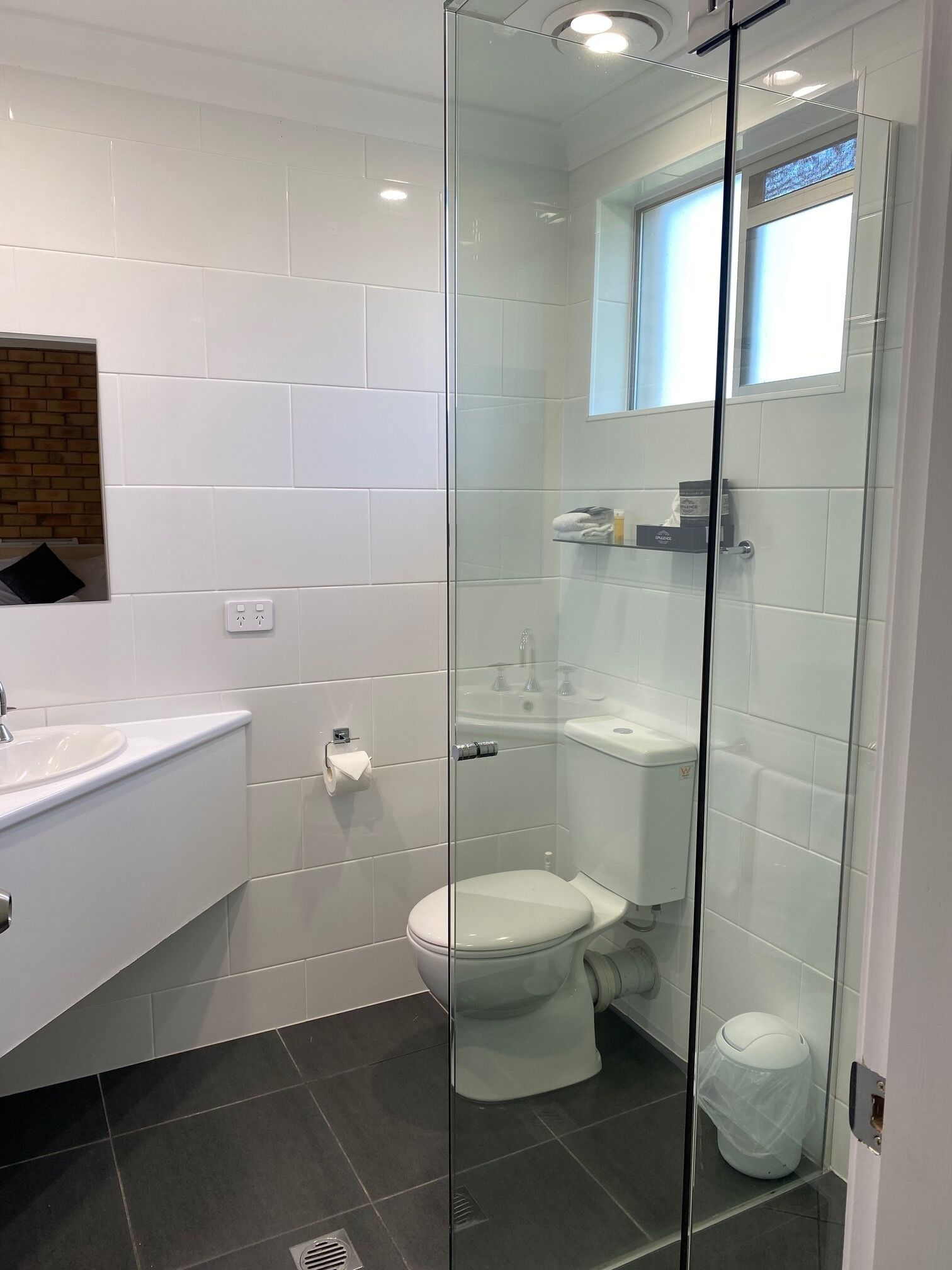 Un baño moderno con ducha de vidrio, inodoro blanco y lavamanos con dispensador de toallas.