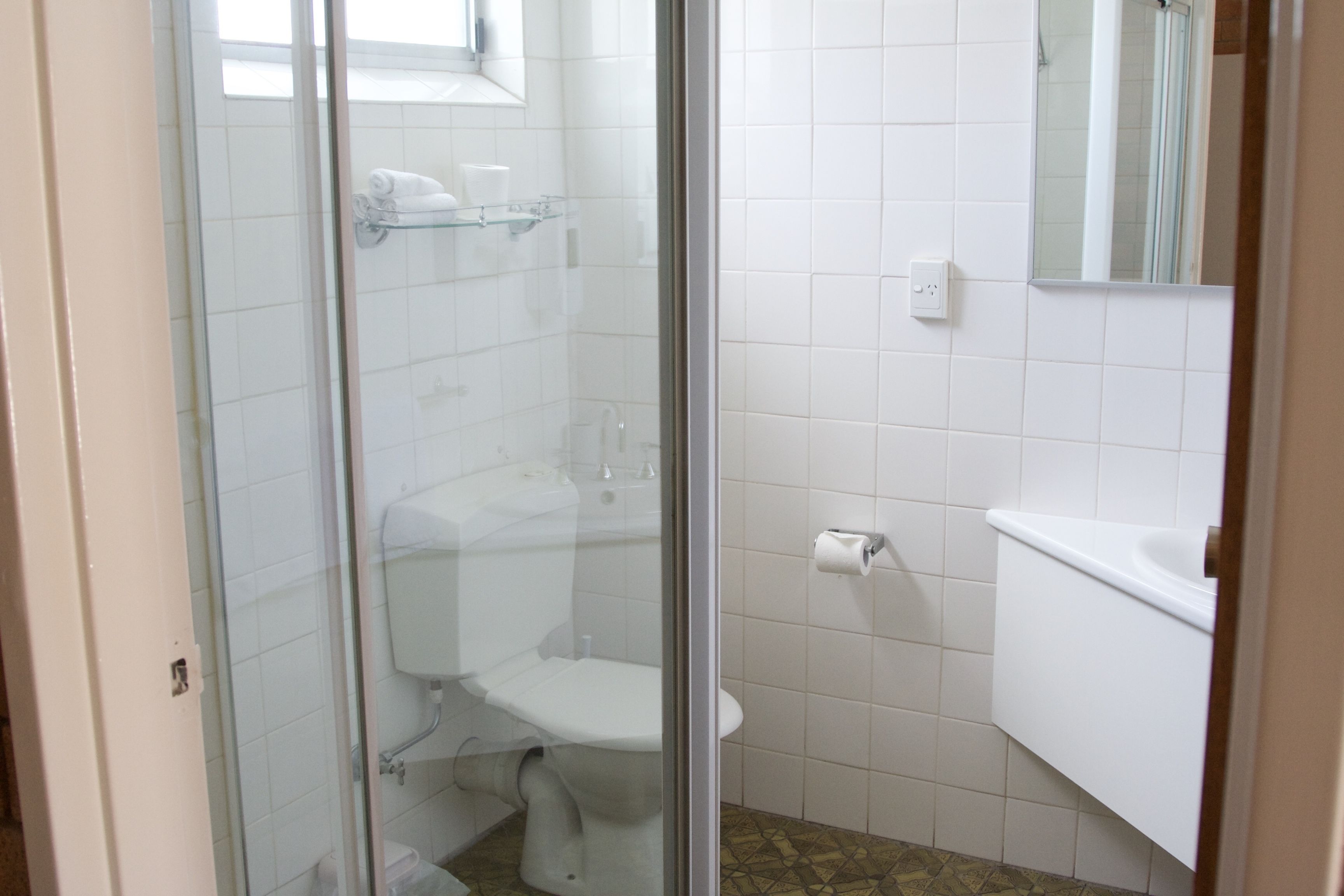 A bathroom with a glass-enclosed shower, a toilet, a sink, and a mirror.