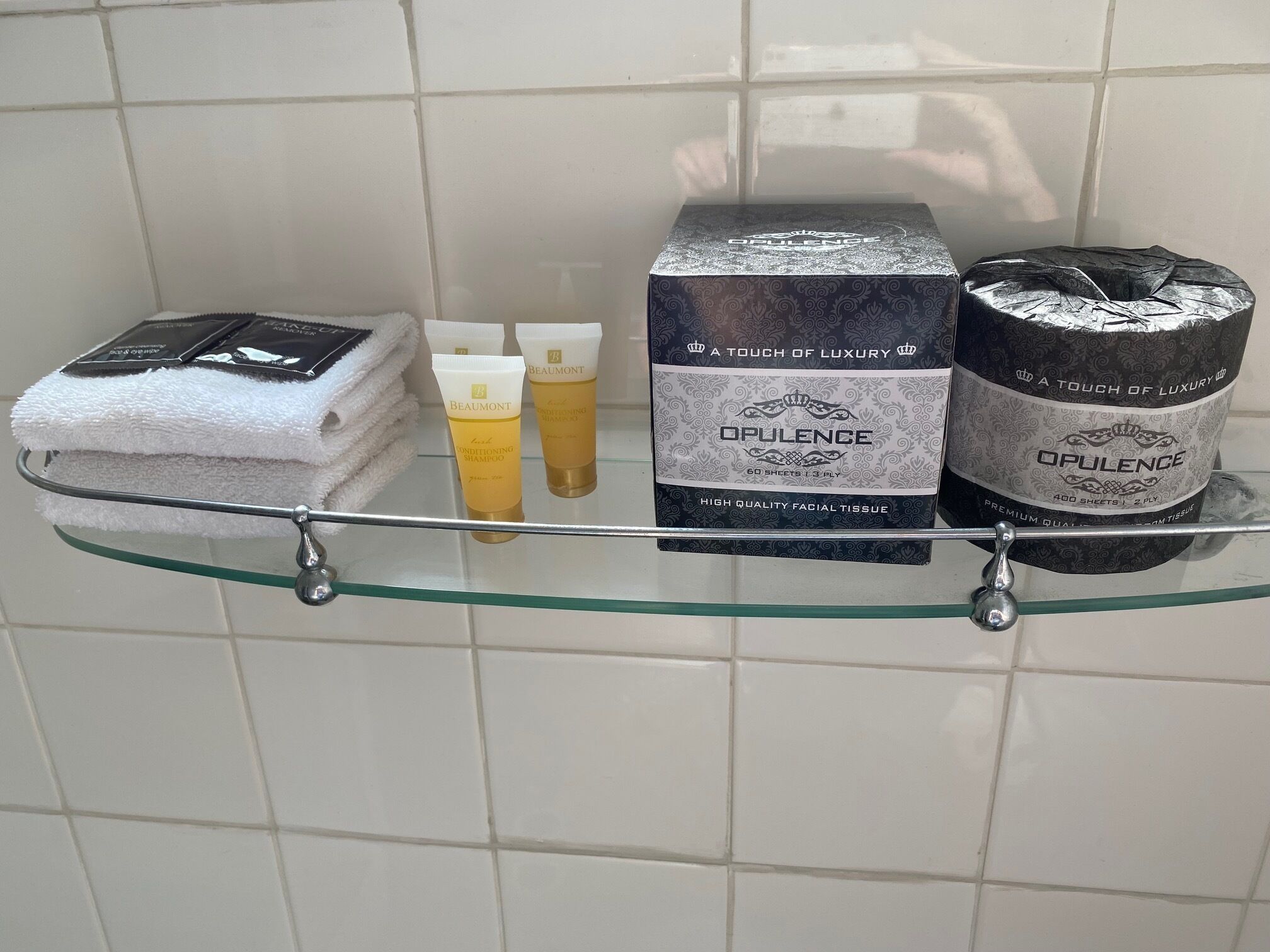 Un estante de baño con artículos de aseo, incluyendo una toalla blanca, dos botellas de champú, una caja de pañuelos faciales y un envase de toallitas faciales.
