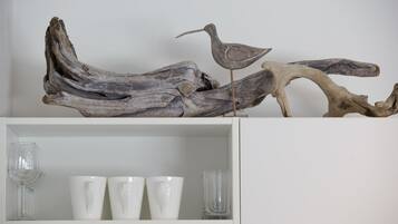 A shelf with three white cups and a glass, and a piece of driftwood with a bird sculpture.