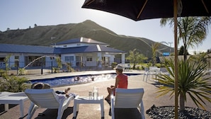 Un espace aménagé au bord de la piscine, avec des chaises longues, une table sur laquelle est posée une carafe, et une vue sur une montagne.