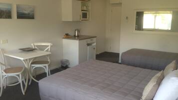Een kleine, schone kamer met een bed, bureau en stoel. Er is een raam met uitzicht op bomen.