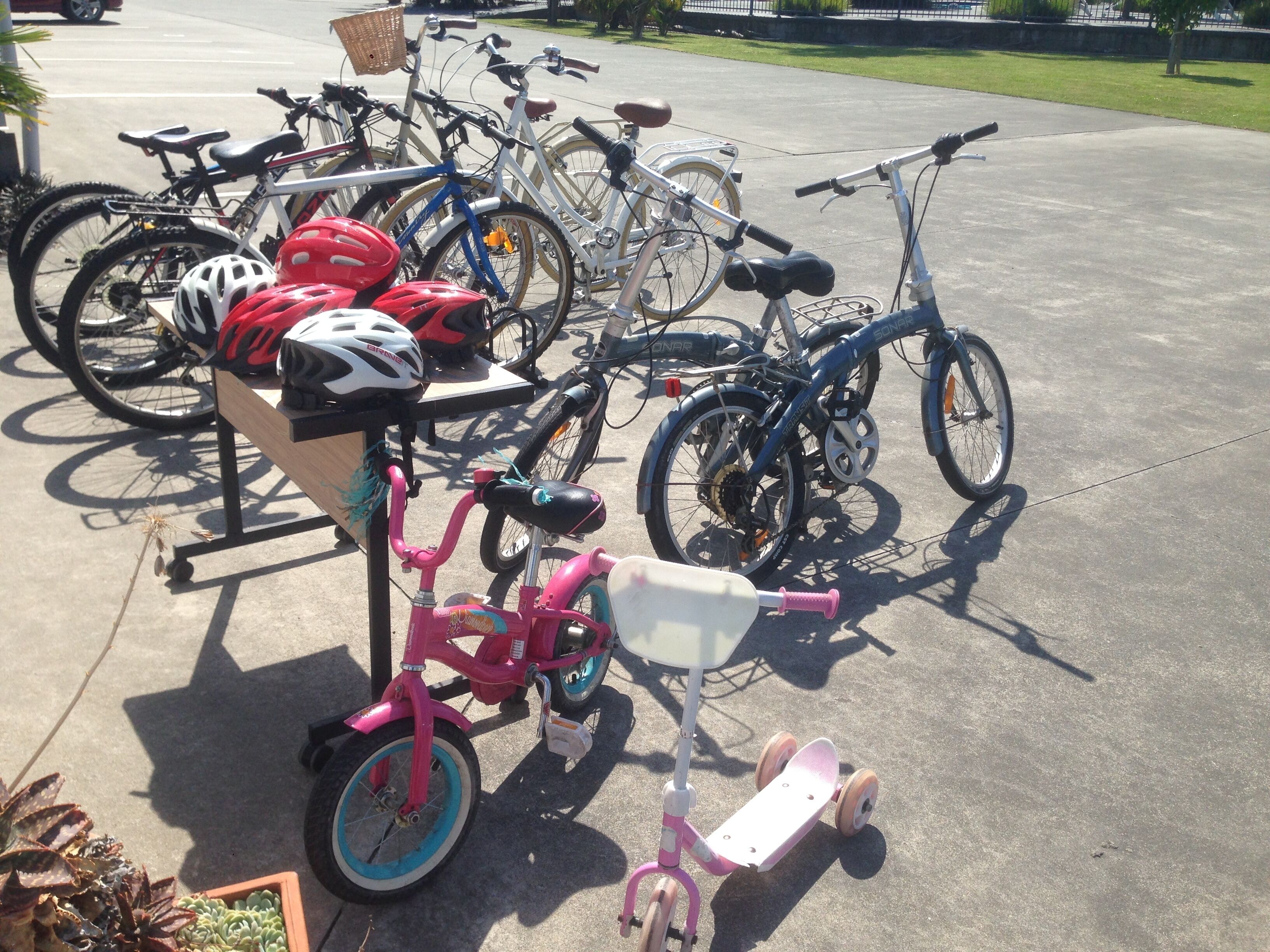 A row of bicycles parked on a concrete surface, with a pink tricycle and a white scooter in the foreground.