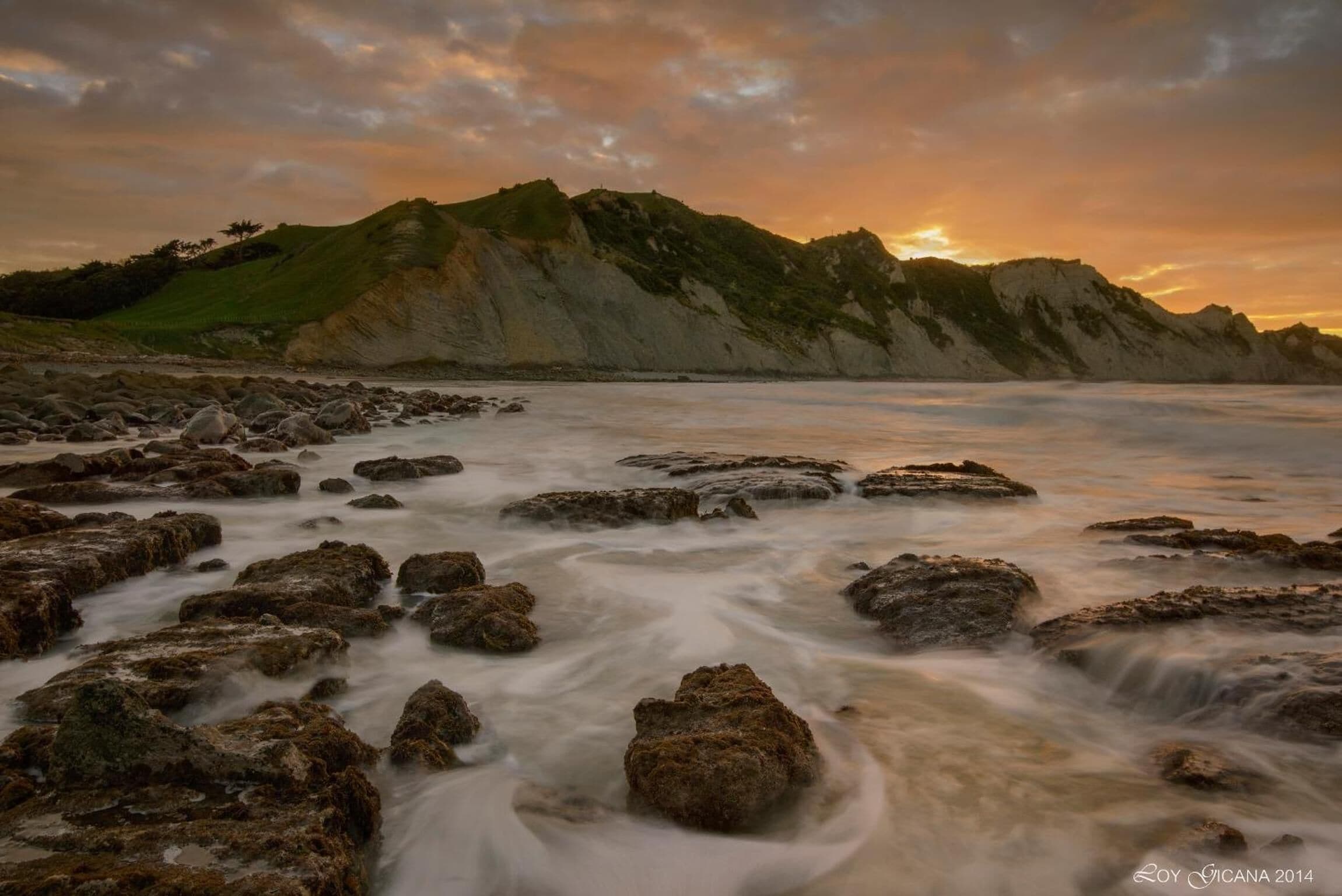A coastal landscape with rocky terrain and a hill in the background.