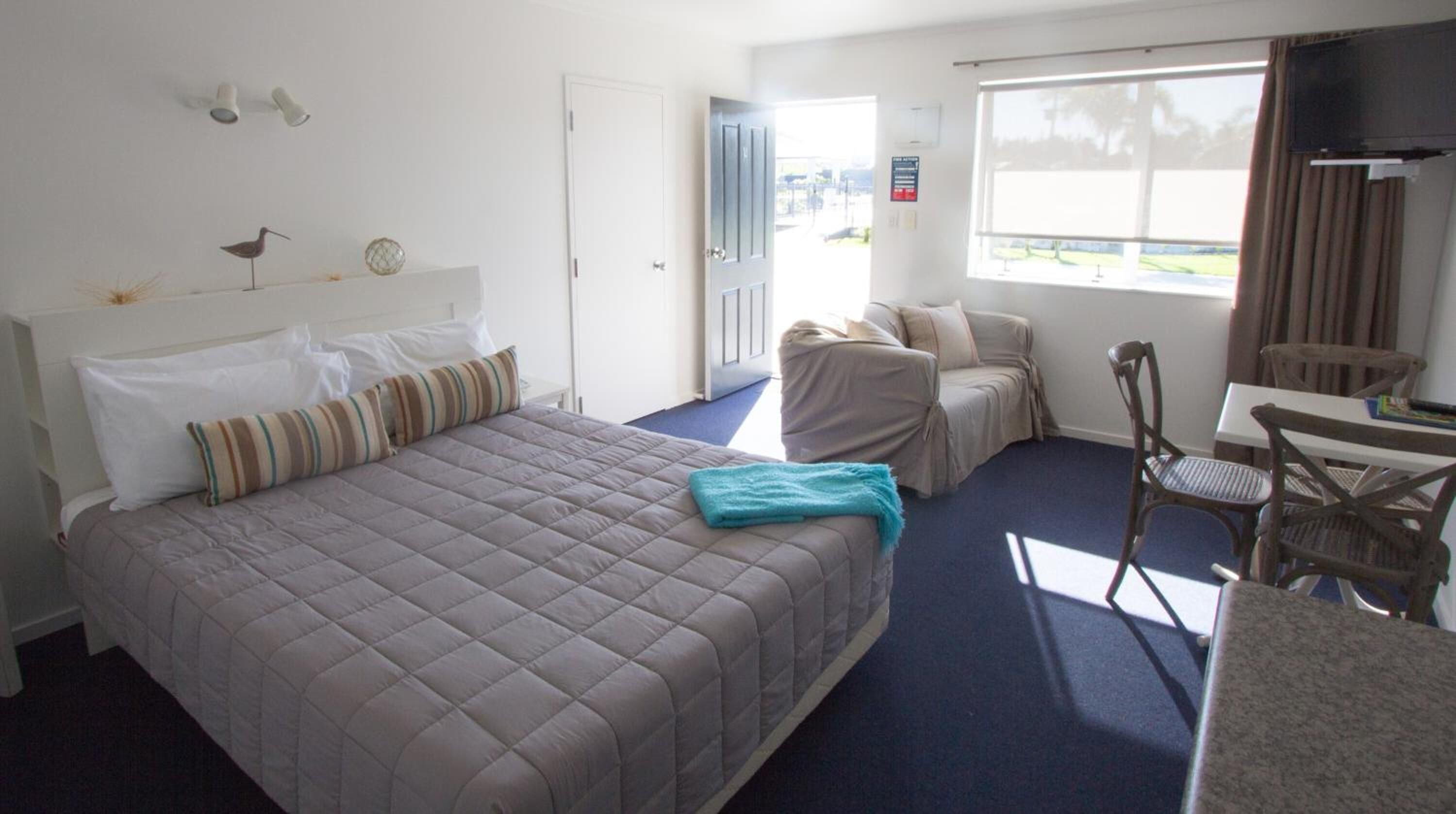 Een hotelkamer met een bed, een bureau, een stoel, een raam met uitzicht en een deur.