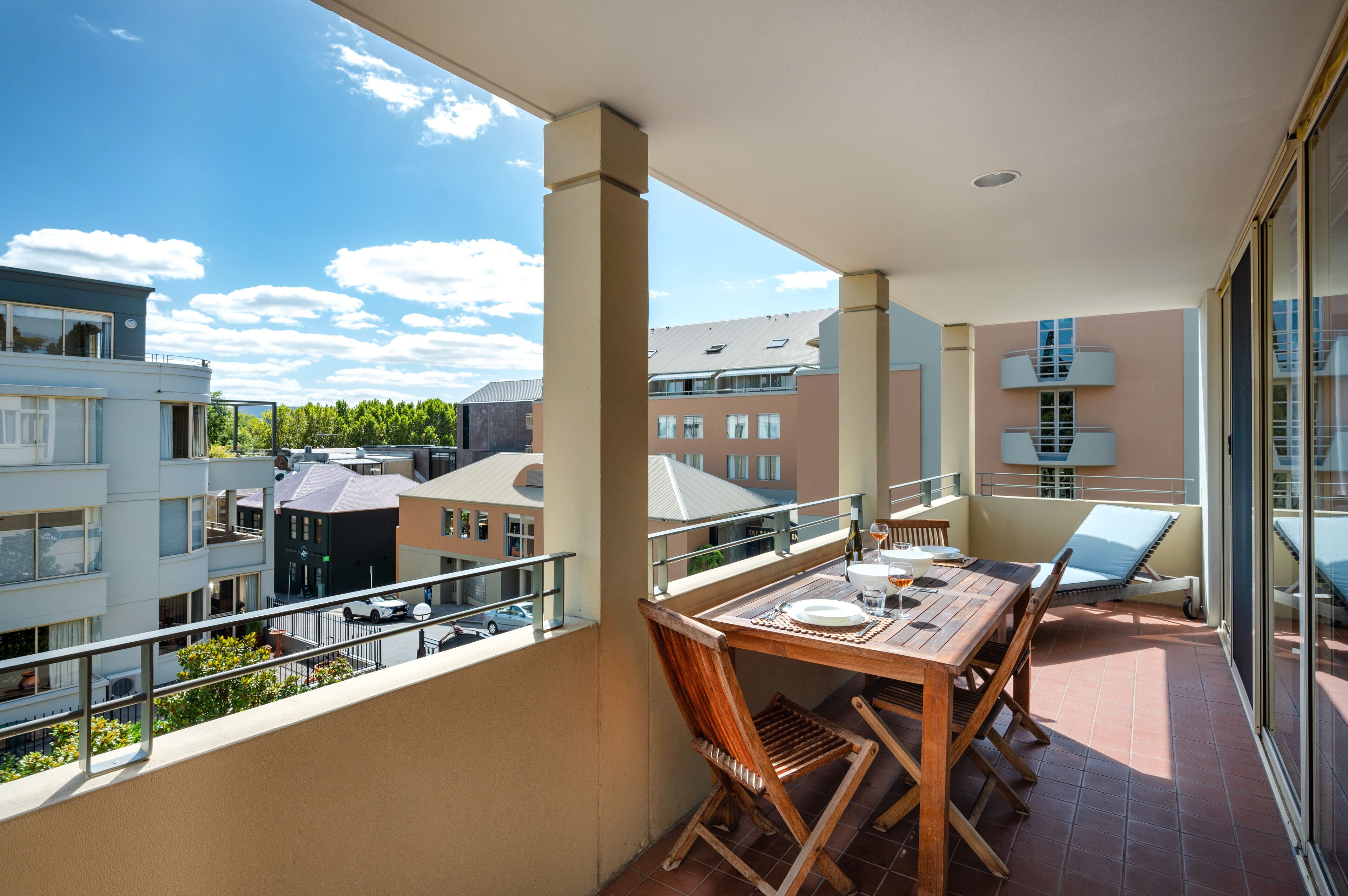 A balcony with a table and chairs, overlooking a residential area with multiple buildings.