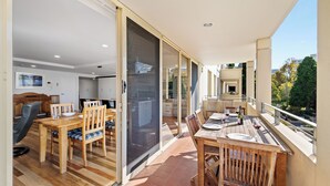 A spacious balcony with a dining area, sliding glass doors leading to a kitchen, and a view of the surrounding area. - Jenatt Apartments Salamanca (Battery Point)