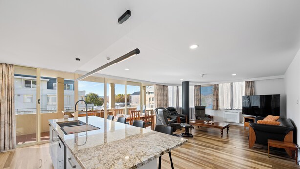 A modern apartment with a kitchen, dining area, and living room. It features large windows, a flat-screen TV, and a comfortable seating area. - Jenatt Apartments Salamanca (Battery Point)