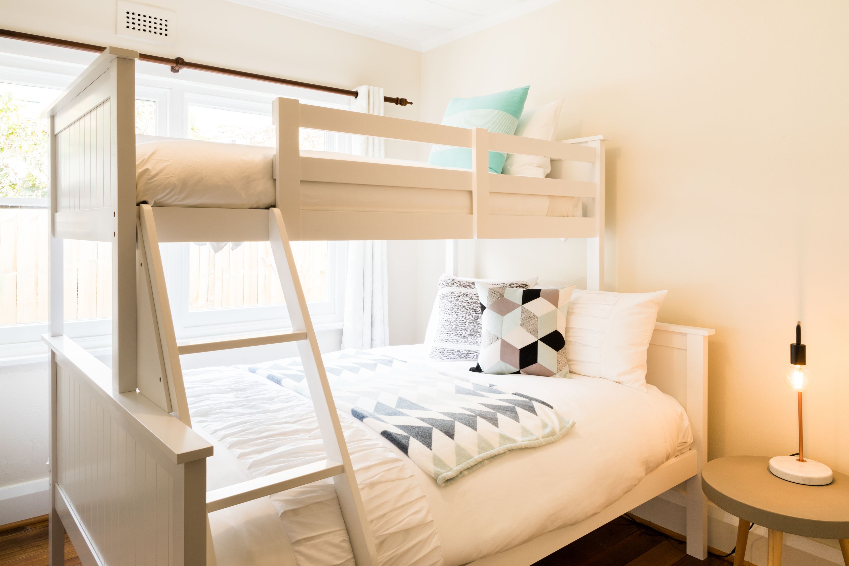 A bunk bed with a white frame and a bedside table with a lamp.