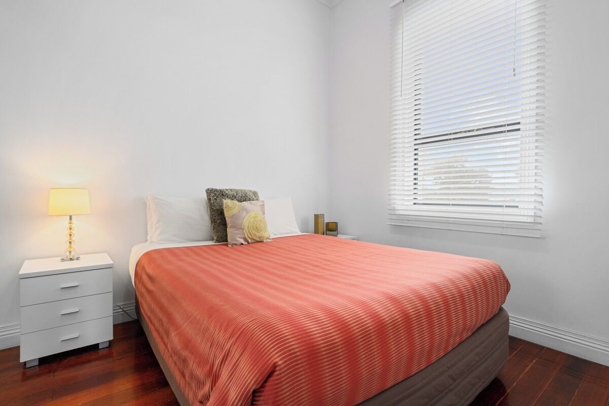 A bedroom with a bed, a nightstand, a lamp, and a window with blinds.